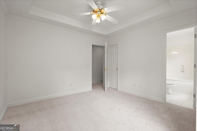 unfurnished bedroom featuring light colored carpet, a raised ceiling, crown molding, baseboards, and ensuite bathroom