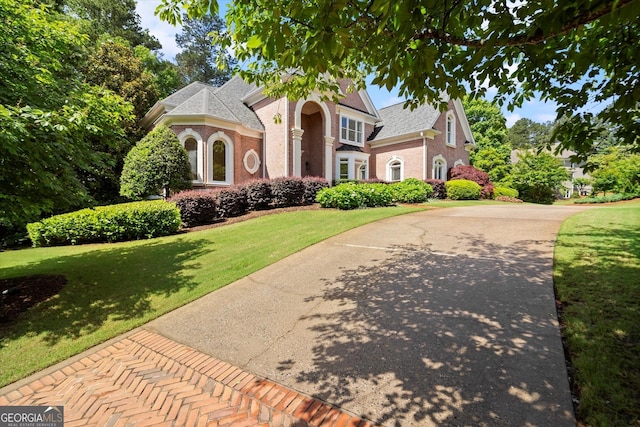 view of front of property with brick siding, a front lawn, driveway, and roof with shingles