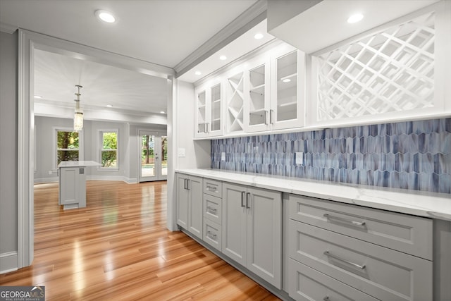 kitchen featuring tasteful backsplash, light wood-type flooring, ornamental molding, glass insert cabinets, and baseboards