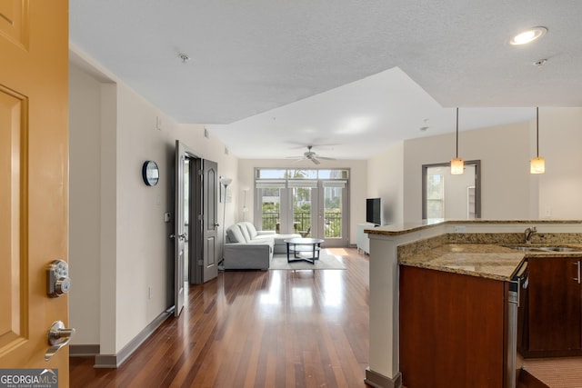 kitchen with a sink, dark wood-style flooring, baseboards, open floor plan, and light stone countertops