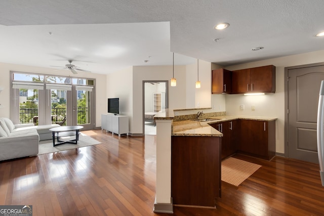 kitchen with open floor plan, a peninsula, a sink, dark wood finished floors, and light stone countertops