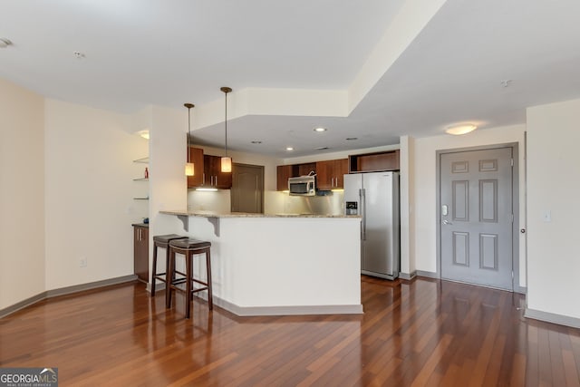 kitchen with appliances with stainless steel finishes, a peninsula, dark wood-type flooring, light stone countertops, and baseboards