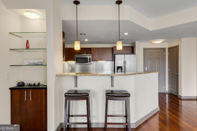kitchen with appliances with stainless steel finishes, dark wood finished floors, a kitchen breakfast bar, a peninsula, and light stone counters