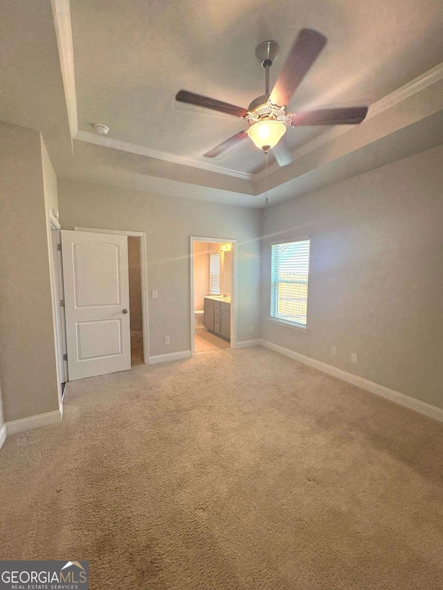 unfurnished bedroom with a raised ceiling, crown molding, light carpet, baseboards, and ensuite bath