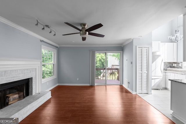 unfurnished living room featuring a ceiling fan, light wood-style floors, crown molding, a brick fireplace, and track lighting