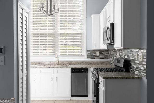 kitchen featuring stainless steel appliances, a sink, white cabinets, a chandelier, and dark stone counters