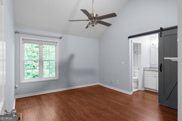 spare room featuring vaulted ceiling, ceiling fan, dark wood-style floors, baseboards, and a barn door