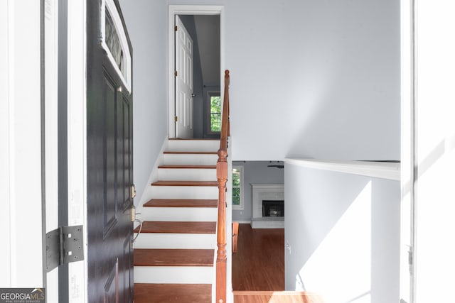 staircase featuring wood finished floors, a brick fireplace, and a high ceiling