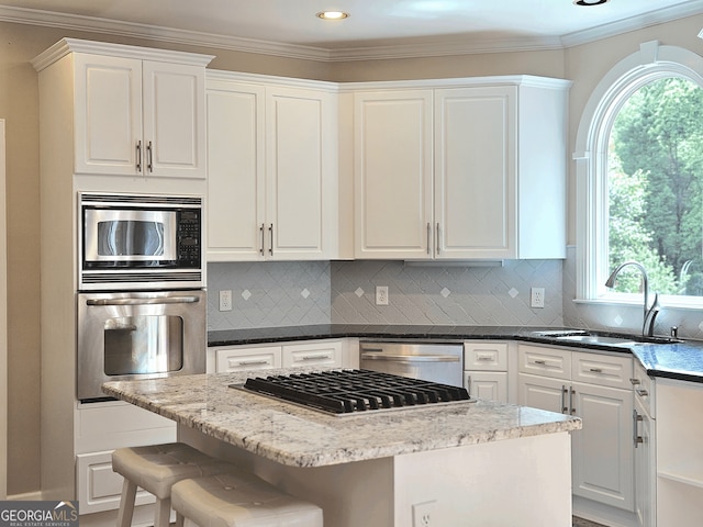 kitchen with appliances with stainless steel finishes, a sink, crown molding, white cabinetry, and a kitchen island