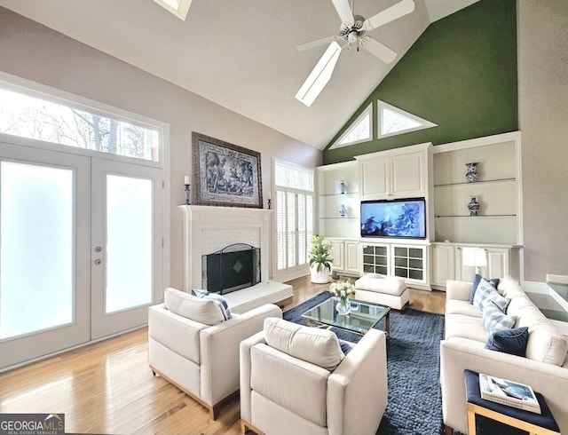 living area featuring high vaulted ceiling, light wood finished floors, french doors, ceiling fan, and a brick fireplace