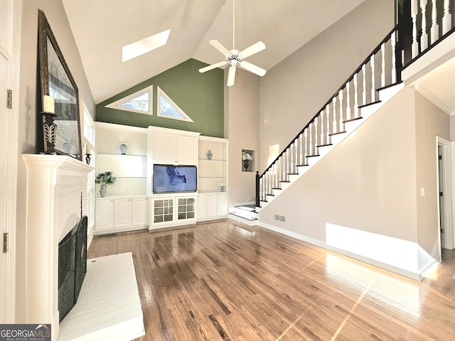 unfurnished living room featuring high vaulted ceiling, wood finished floors, ceiling fan, stairway, and a brick fireplace