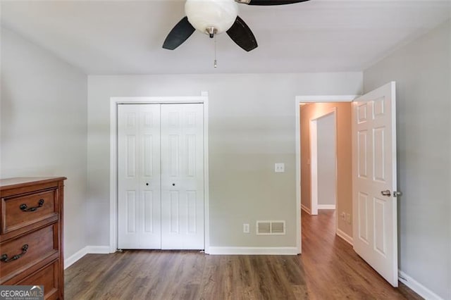unfurnished bedroom featuring wood finished floors, a closet, baseboards, and a ceiling fan