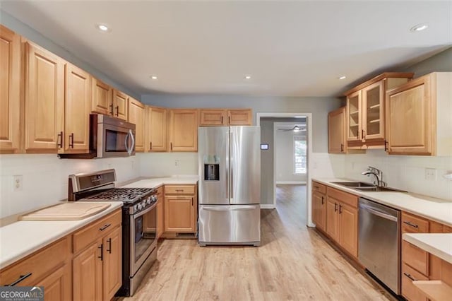 kitchen with appliances with stainless steel finishes, a sink, light wood-style floors, glass insert cabinets, and light countertops