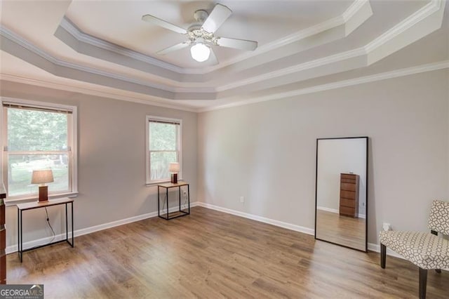 spare room with a raised ceiling, wood finished floors, crown molding, ceiling fan, and baseboards