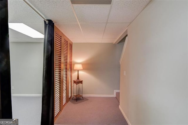 hall featuring a drop ceiling, carpet flooring, and baseboards