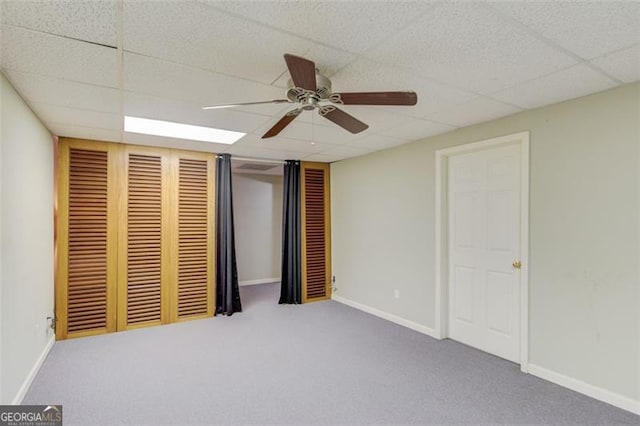 unfurnished bedroom featuring a closet, carpet flooring, a drop ceiling, baseboards, and ceiling fan