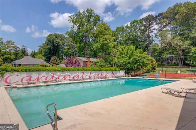 community pool featuring fence, a patio, and view of wooded area