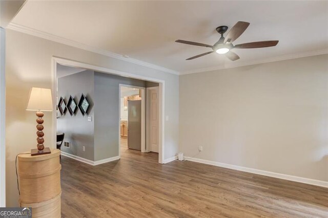 empty room featuring crown molding, ceiling fan, wood finished floors, and baseboards