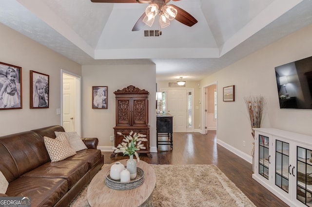 living area with dark wood-type flooring, a ceiling fan, lofted ceiling, baseboards, and a raised ceiling