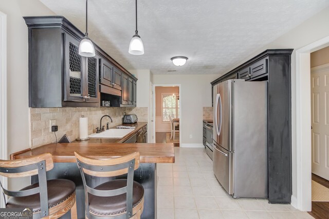 kitchen featuring stainless steel appliances, a sink, decorative backsplash, baseboards, and hanging light fixtures