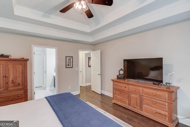 bedroom featuring crown molding, a tray ceiling, dark wood-style floors, baseboards, and a ceiling fan
