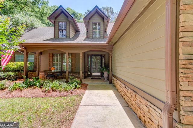 doorway to property featuring covered porch and roof with shingles