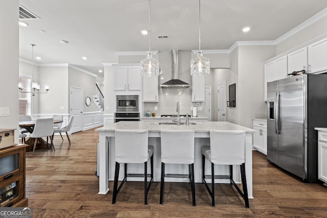 kitchen with stainless steel appliances, wall chimney exhaust hood, ornamental molding, a kitchen island with sink, and a sink