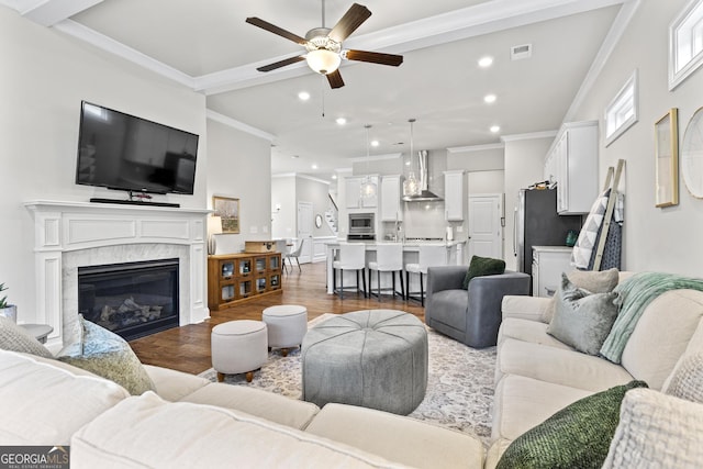 living area with a ceiling fan, crown molding, wood finished floors, recessed lighting, and a glass covered fireplace