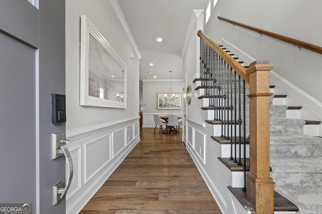 entryway with stairway, crown molding, a decorative wall, wainscoting, and dark wood finished floors
