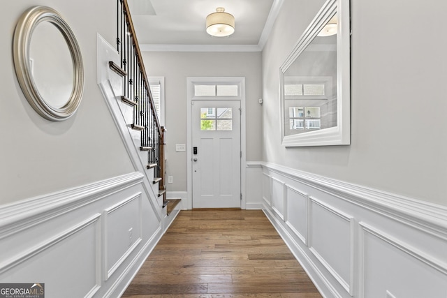 entryway featuring stairs, ornamental molding, a wainscoted wall, wood finished floors, and a decorative wall