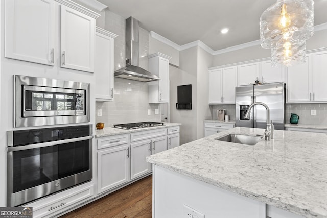kitchen with stainless steel appliances, wall chimney exhaust hood, white cabinetry, a sink, and crown molding