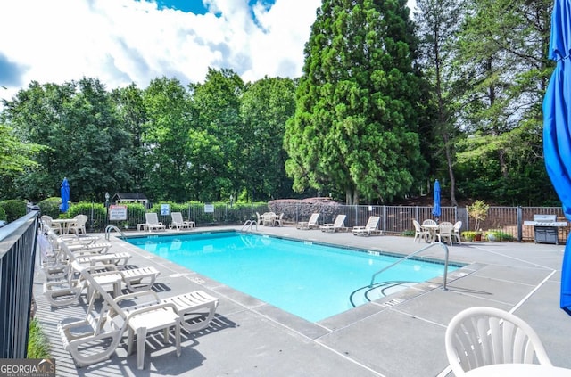 community pool with fence, a patio area, and view of wooded area