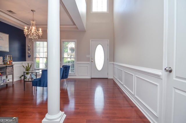 entryway with ornate columns, a wainscoted wall, a decorative wall, a chandelier, and wood finished floors