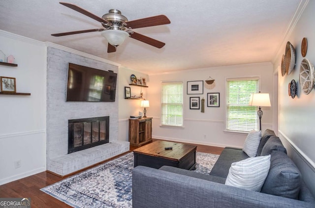 living area with a brick fireplace, wood finished floors, ceiling fan, crown molding, and baseboards