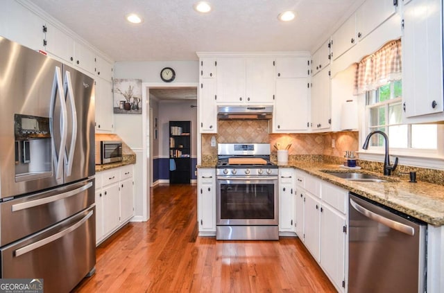 kitchen featuring appliances with stainless steel finishes, a sink, under cabinet range hood, white cabinetry, and recessed lighting