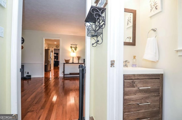 hallway featuring dark wood-type flooring, crown molding, and a sink