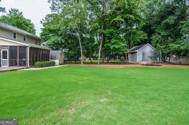 view of yard featuring a trampoline, a storage shed, an outbuilding, a sunroom, and view of wooded area