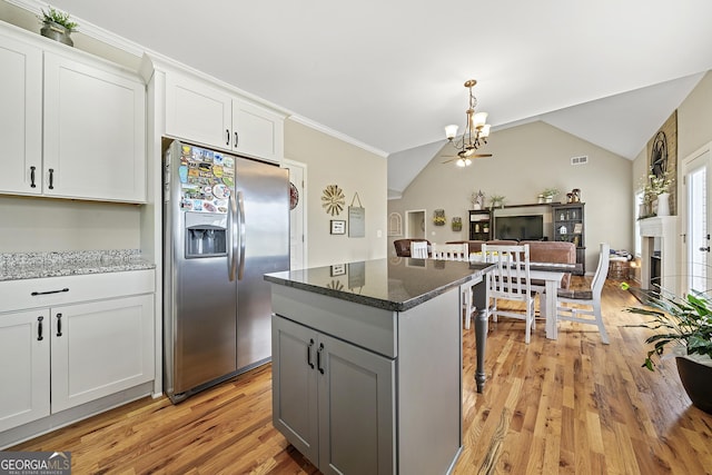 kitchen with stainless steel refrigerator with ice dispenser, a chandelier, a center island, light wood-style floors, and open floor plan