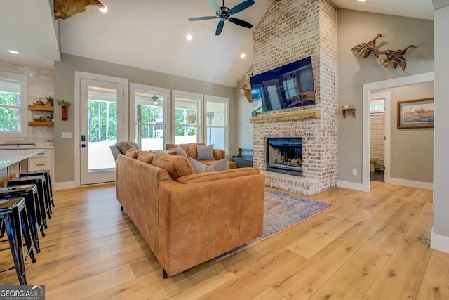 living room with a ceiling fan, a fireplace, high vaulted ceiling, light wood-style floors, and baseboards