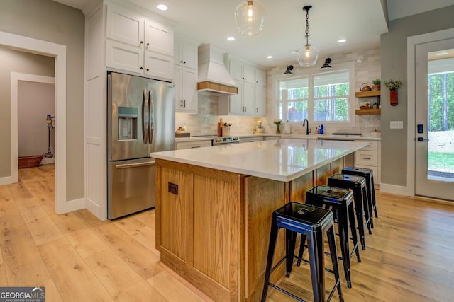 kitchen with stainless steel appliances, custom range hood, backsplash, white cabinets, and a kitchen island