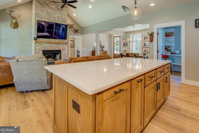 kitchen with open floor plan, light wood-style floors, a brick fireplace, a center island, and recessed lighting