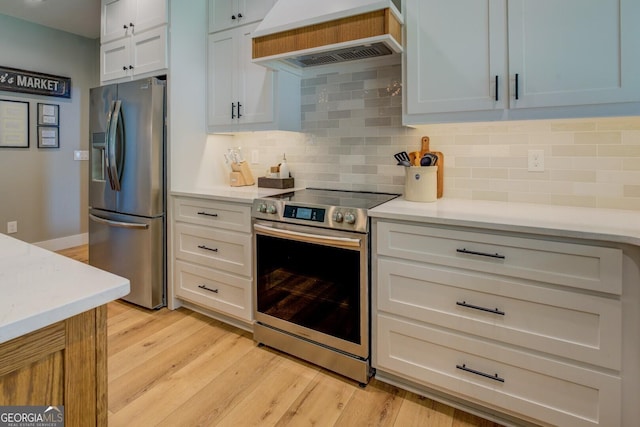 kitchen with appliances with stainless steel finishes, custom exhaust hood, light countertops, light wood-style flooring, and tasteful backsplash