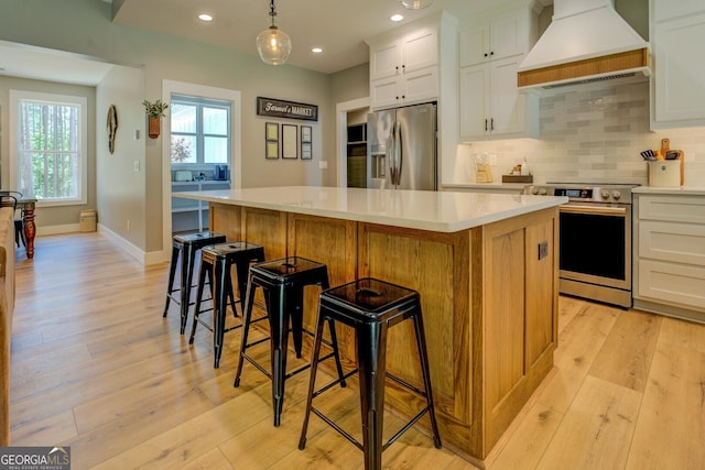 kitchen featuring appliances with stainless steel finishes, premium range hood, a kitchen island, light wood-style flooring, and recessed lighting