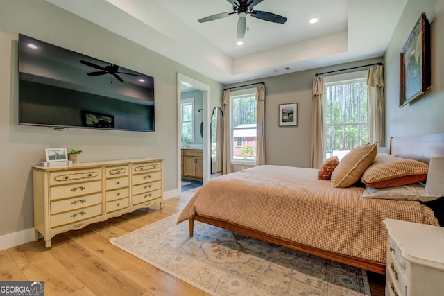 bedroom with light wood-type flooring, baseboards, a tray ceiling, recessed lighting, and ensuite bathroom