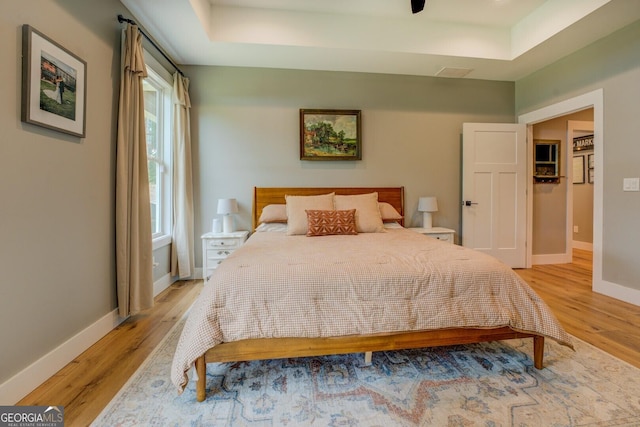 bedroom with light wood-style flooring, baseboards, and a tray ceiling