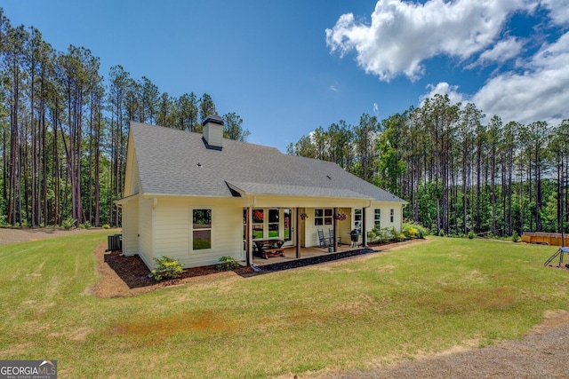 back of property featuring a yard, a chimney, a patio area, and roof with shingles