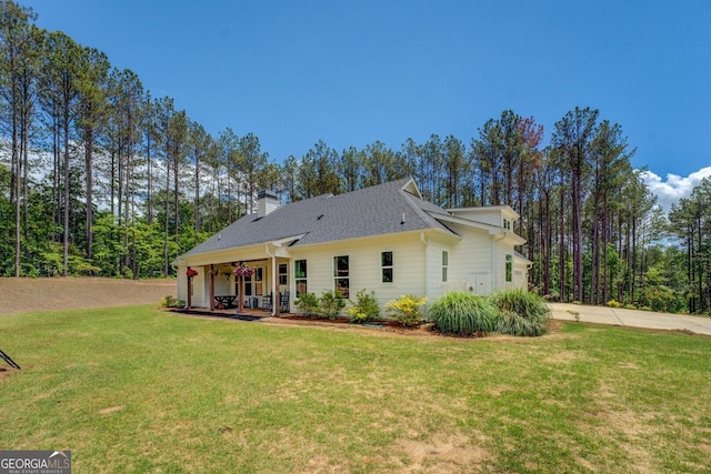 back of house with a lawn, a chimney, and roof with shingles