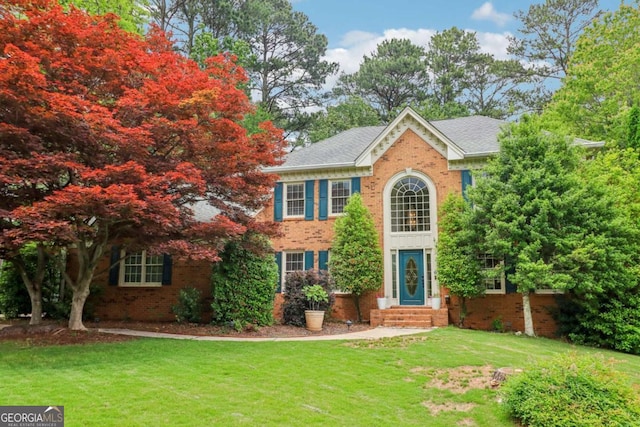 colonial-style house featuring brick siding, entry steps, and a front yard