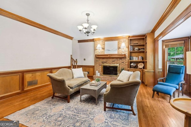 living area featuring a chandelier, light wood-style floors, ornamental molding, wainscoting, and a brick fireplace
