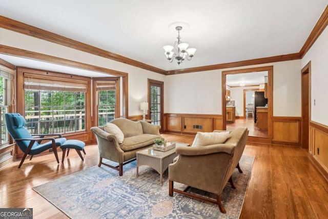 living area with wainscoting, a chandelier, plenty of natural light, wood finished floors, and crown molding